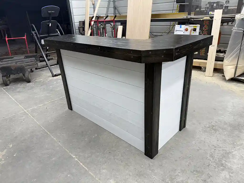 Workbench-style bar counter with a dark wood top and light gray paneled sides in a cluttered workshop.