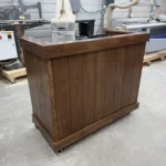 Walnut color Mobile Hostess Stand with 3 shelves 1 Wooden bar or counter on caster wheels in a workshop with machines in the background.
